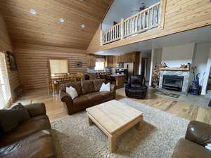 Living room featuring a ceiling fan, high vaulted ceiling, log walls, a fireplace, and light wood-style floors