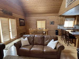 Living room with light wood-style flooring, wood ceiling, high vaulted ceiling, and log walls