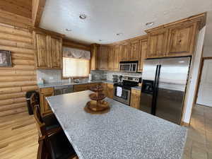 Kitchen with recessed lighting, a textured ceiling, appliances with stainless steel finishes, and brown cabinetry