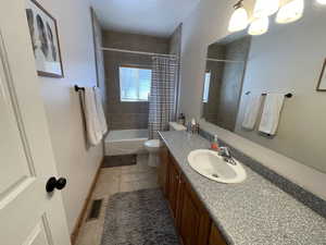 Bathroom featuring visible vents, shower / bathtub combination with curtain, toilet, baseboards, and vanity