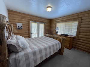 Bedroom featuring log walls, carpet floors, and a textured ceiling