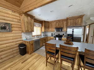 Kitchen with light wood-style flooring, a sink, stainless steel appliances, brown cabinetry, and decorative backsplash