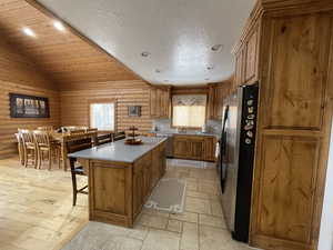Kitchen featuring brown cabinetry, vaulted ceiling, appliances with stainless steel finishes, a kitchen breakfast bar, and a center island