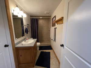 Full bath with baseboards, toilet, vanity, a stall shower, and a textured ceiling