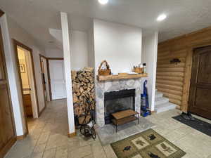 Living room with baseboards, a fireplace, rustic walls, stone tile flooring, and a textured ceiling