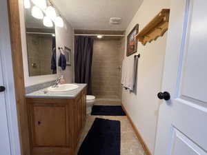 Full bathroom with toilet, a textured ceiling, tiled shower, baseboards, and vanity