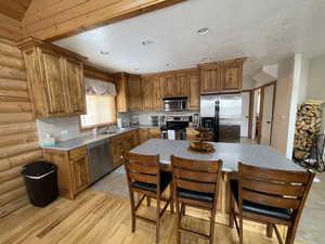 Kitchen with brown cabinetry, stainless steel appliances, log walls, and tasteful backsplash