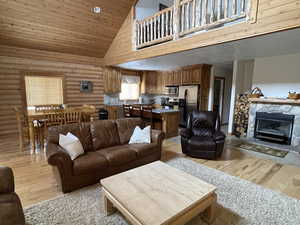 Living room with a stone fireplace, high vaulted ceiling, light wood-style floors, and log walls