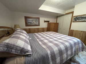 Bedroom with wooden walls, wainscoting, a closet, and a textured ceiling