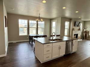 Kitchen featuring a sink, dark countertops, dark wood finished floors, a fireplace, and dishwasher