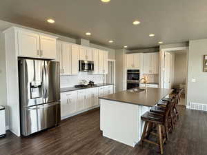 Kitchen with dark countertops, visible vents, dark wood finished floors, stainless steel appliances, and white cabinetry