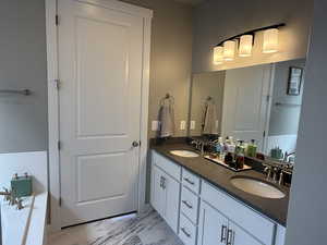 Full bath featuring double vanity, a bath, marble finish floor, and a sink