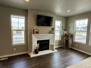 Unfurnished living room featuring hardwood / wood-style flooring, baseboards, visible vents, and a fireplace with raised hearth