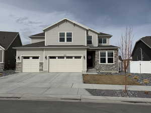 View of front facade with stone siding, driveway, an attached garage, and fence