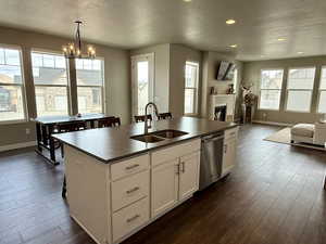 Kitchen featuring a center island with sink, a sink, dark countertops, open floor plan, and dishwasher