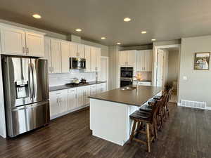 Kitchen with dark wood-style flooring, dark countertops, visible vents, and appliances with stainless steel finishes
