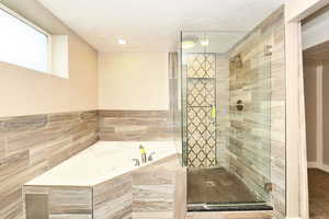 Full bathroom featuring a shower stall, a garden tub, and a textured ceiling