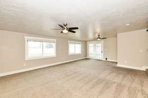 Carpeted spare room with a ceiling fan, baseboards, and a textured ceiling