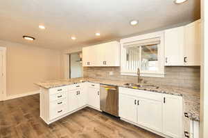 Kitchen with dishwasher, a peninsula, dark wood finished floors, and a sink