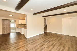 Unfurnished living room featuring beamed ceiling, visible vents, wood finished floors, baseboards, and stairs