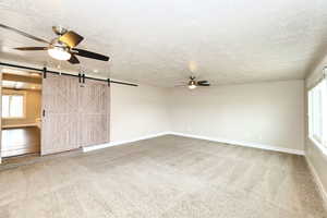 Carpeted spare room featuring a barn door, a textured ceiling, baseboards, and a ceiling fan