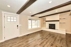 Unfurnished living room featuring a glass covered fireplace, baseboards, beam ceiling, and wood finished floors