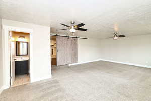 Unfurnished living room featuring a sink, a barn door, carpet, and ceiling fan