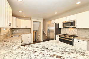 Kitchen with a sink, light stone counters, appliances with stainless steel finishes, and white cabinets