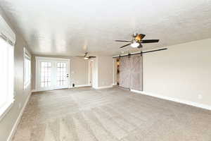 Unfurnished living room featuring a textured ceiling, a barn door, carpet flooring, baseboards, and ceiling fan