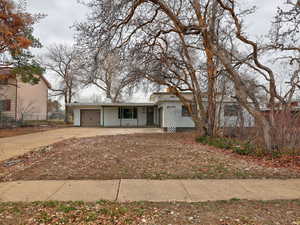 View of front of property featuring a garage, brick siding, driveway, and fence