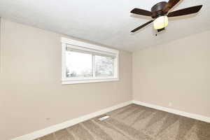 Carpeted spare room featuring visible vents, baseboards, a textured ceiling, and ceiling fan