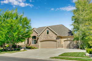 View of front facade with stone siding, concrete driveway, a garage, and roof with shingles