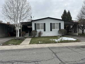 Manufactured / mobile home with a carport, concrete driveway, and a front lawn