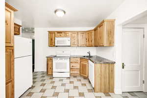 Kitchen with white appliances, a sink, dark countertops, and baseboards