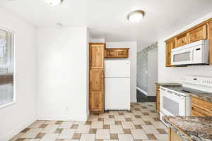 Kitchen with white appliances, baseboards, and dark countertops