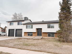 View of front of house with concrete driveway, an attached garage, brick siding, and a chimney