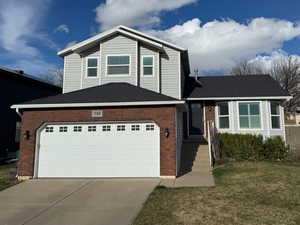 Tri-level home featuring brick siding, driveway, an attached garage, and a front yard