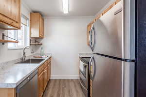 Kitchen featuring light wood finished floors, light countertops, ornamental molding, stainless steel appliances, and a sink