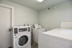 Common laundry area with washer and dryer, visible vents, and dark wood-style flooring