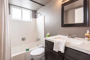 Bathroom with toilet, vanity, and shower / bathtub combination with curtain