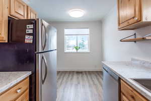 Kitchen with crown molding, baseboards, light brown cabinetry, appliances with stainless steel finishes, and light wood-style floors