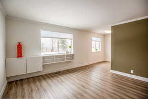 Spare room featuring visible vents, crown molding, baseboards, and wood finished floors