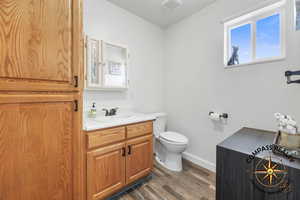1/2 Bathroom featuring visible vents, baseboards, toilet, wood finished floors, and vanity