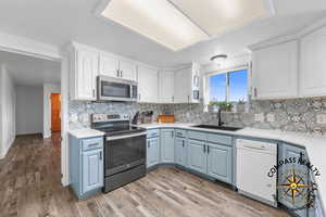Kitchen featuring a sink, blue cabinets, appliances with stainless steel finishes, and white cabinetry