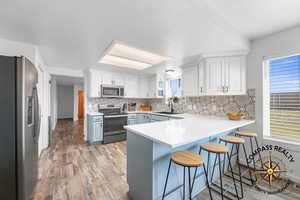 Kitchen with a peninsula, a sink, appliances with stainless steel finishes, a kitchen bar, and tasteful backsplash