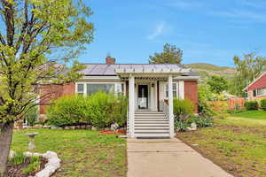 Bungalow-style home featuring roof mounted solar panels, a chimney, and fence