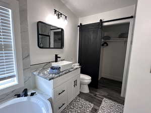 Full bath featuring toilet, a tub to relax in, a textured ceiling, wood finished floors, and vanity