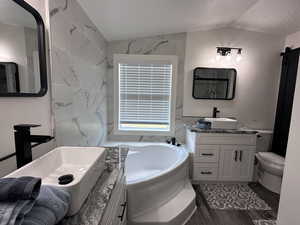 Full bathroom featuring a garden tub, two vanities, a sink, a textured ceiling, and vaulted ceiling