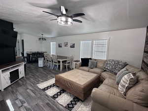 Living room with wood finished floors, ceiling fan with notable chandelier, and a textured ceiling