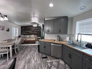 Kitchen featuring butcher block countertops, lofted ceiling, gray cabinets, stainless steel dishwasher, and a sink